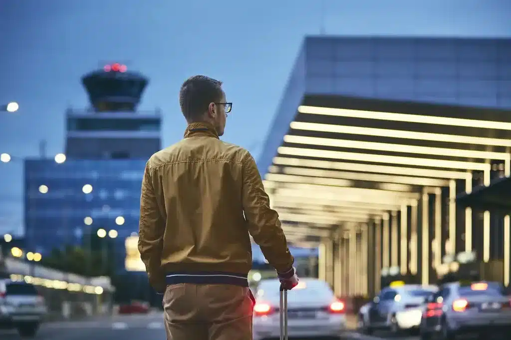 Voyageur avec sa valise à la sortie de l'aéroport, au crépuscule, avant son VTC pour Bordeaux