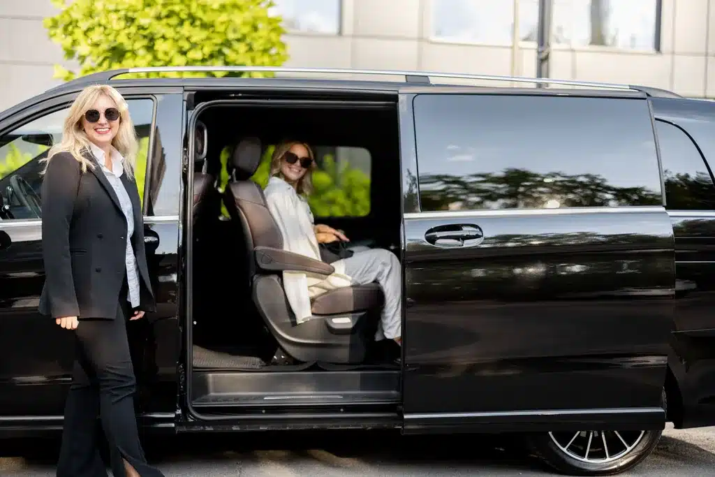 Chauffeuse VTC qui ouvre la portière du van noir à sa passagère, à Bruges